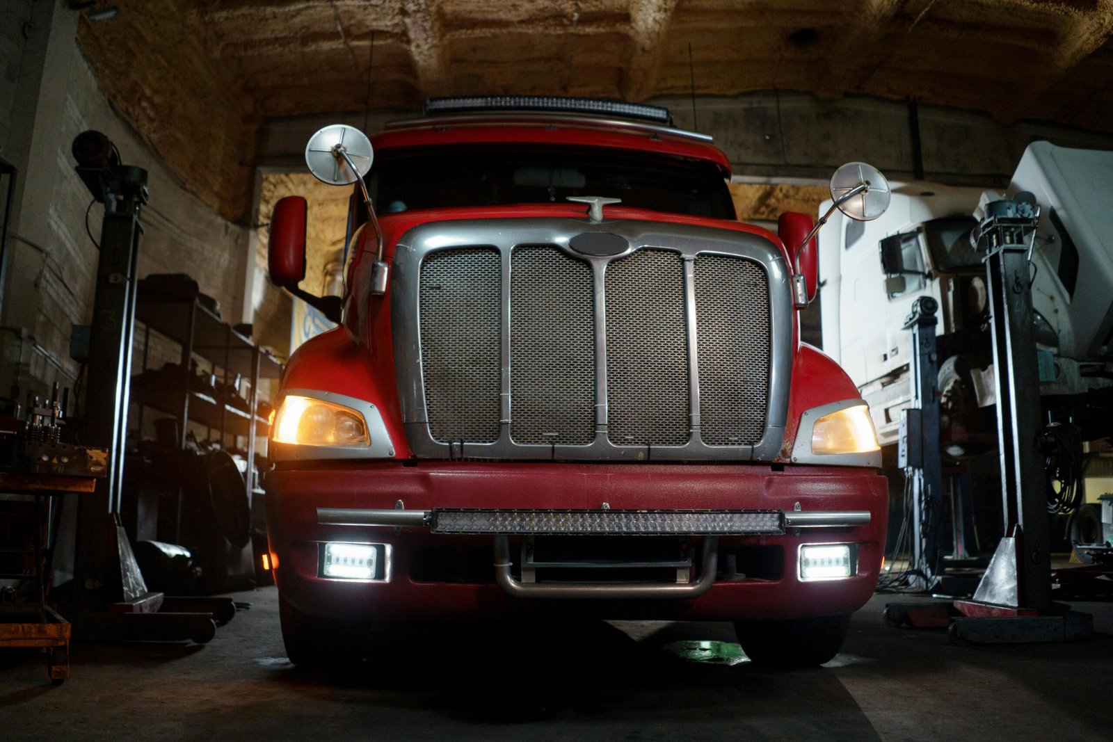Front view of a red truck in a dimly lit automotive repair shop with a focus on the grill and headlights.